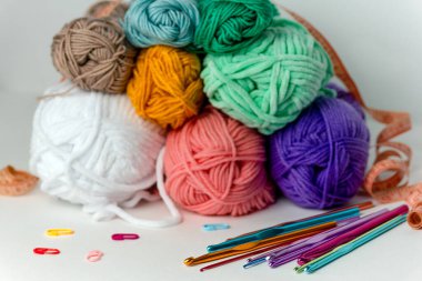 Beyaz arka planda farklı çapta çok renkli örgü kancaları, iplik izleri ve turuncu santimetre şeritlerin yanında. Yatay bir arkaplanda. Hobi, el yapımı, el işi.