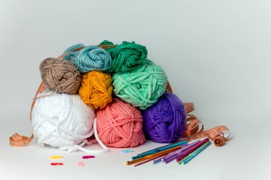 Beyaz arka planda farklı çapta çok renkli örgü kancaları, iplik izleri ve turuncu santimetre şeritlerin yanında. Yatay bir arkaplanda. Hobi, el yapımı, el işi.