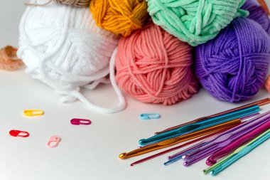 Beyaz arka planda farklı çapta çok renkli örgü kancaları, iplik izleri ve turuncu santimetre şeritlerin yanında. Yatay bir arkaplanda. Hobi, el yapımı, el işi.