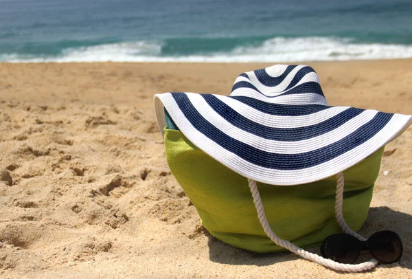 Green beach bag on the seacoast and striped straw hat — Stock Photo, Image