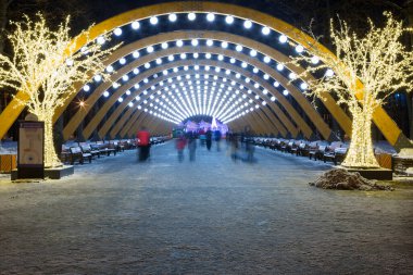 Moskova, Rusya - 18 Aralık 2021: Sokolniki Parkı 'nda Noel Işığı kemeri. Akşamları, insanlar Sokolniki Parkı 'ndaki aydınlık kemerli sokakta yürürler..