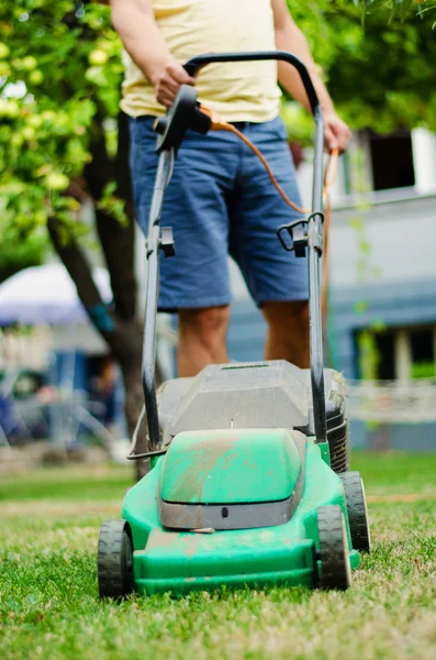 Man moves with lawnmower & mows green grass — Stock Photo, Image