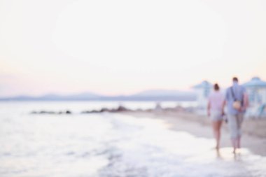 Çiftin sahilde yürürken çekilmiş bulanık bir fotoğrafı. Romantik Çift Sahilde Güzel Günbatımı Yürüyüşü Yapıyor.