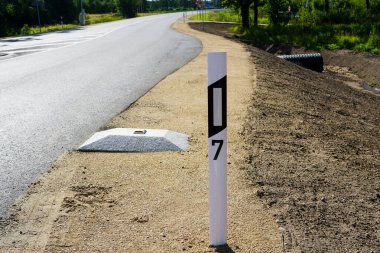 Yansıtıcılı plastik yol direğiyle yeniden inşa edilmiş yol kenarı ve yansıtıcı bir yol çivisi ile beton hız tümseği