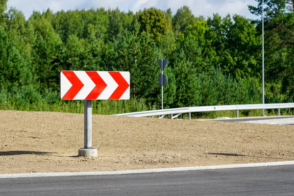 a reflective direction road sign with red and white arrows before a dangerous turn