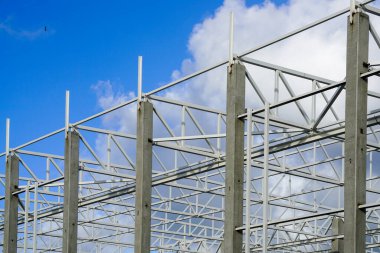 Mavi gökyüzüne karşı tamamlanmamış modern bir endüstriyel binanın metal iskeleti.