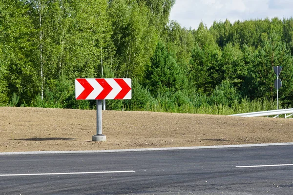 Tehlikeli bir dönemeçten önce kırmızı ve beyaz okları olan yansıtıcı bir yol işareti.