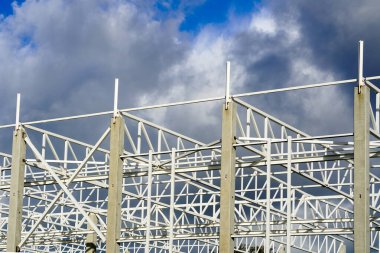 Mavi gökyüzüne karşı tamamlanmamış modern bir endüstriyel binanın metal iskeleti.