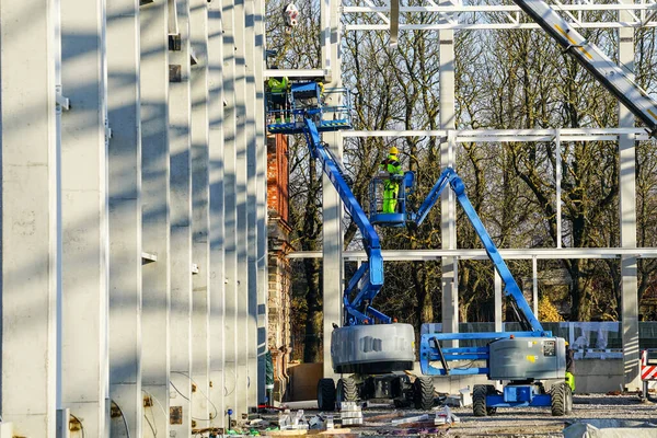 Üniformalı işçilerle itmeli makas platformları ve metal inşaat iskeleti montajı ve montajında güvenlik önleyici ekipmanlar.