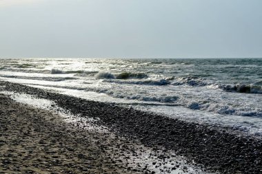 sandy sea coastline with pebbles against the sunlight