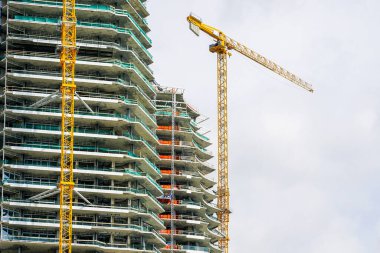 Sarı bir kule vinci ve tamamlanmamış bir beton bina ya da gökdelenin ön cephesinin bir parçası.