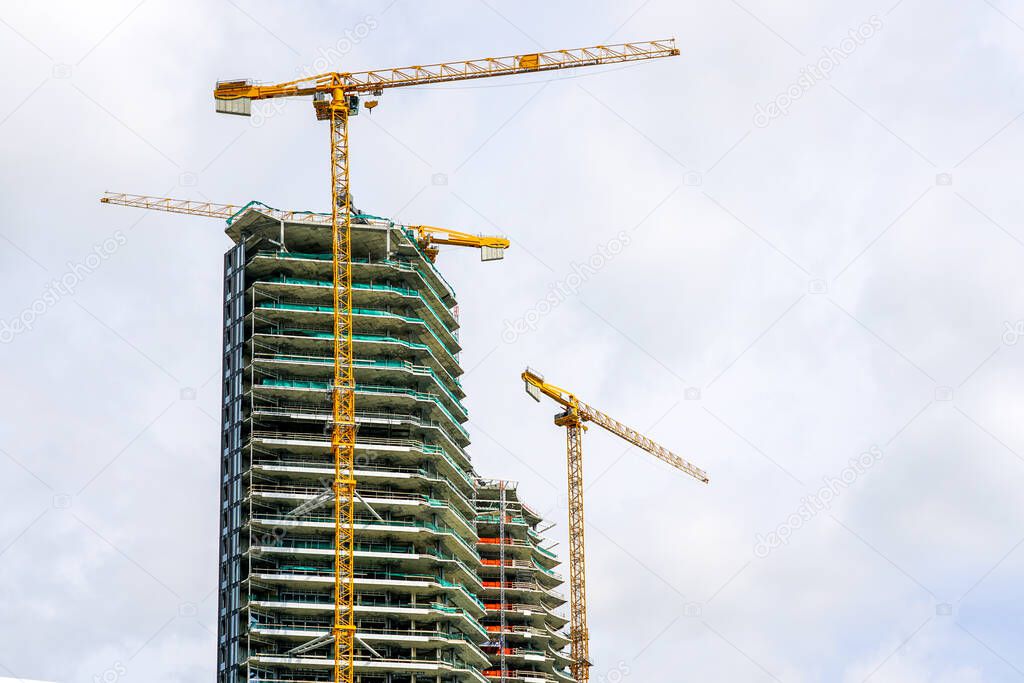 three yellow tower cranes and a fragment of the facade of an unfinished cement building or skyscraper