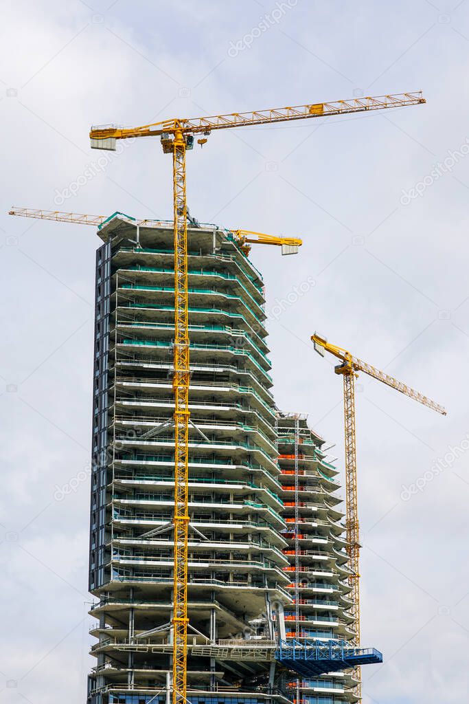 three yellow tower cranes and a fragment of the facade of an unfinished cement building or skyscraper
