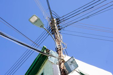 Bir sürü bağlı kablo, kablo ve mavi gökyüzü arka planında LED sokak feneri ile ahşap elektrik direği