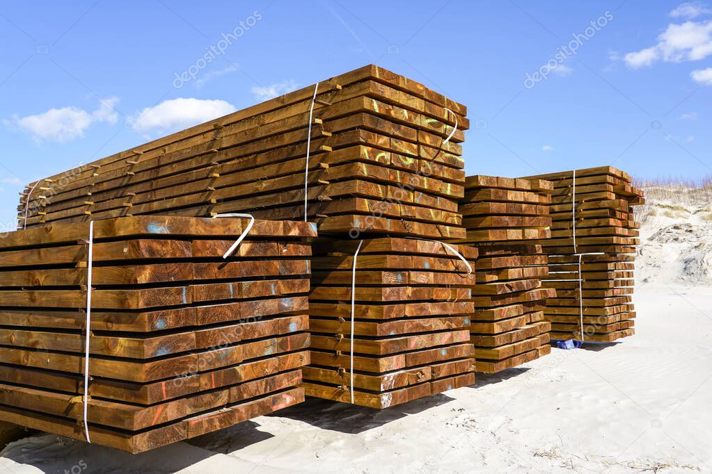 Stacked impregnated brown pine wood boards by the sea on a sandy beach, blue sky background