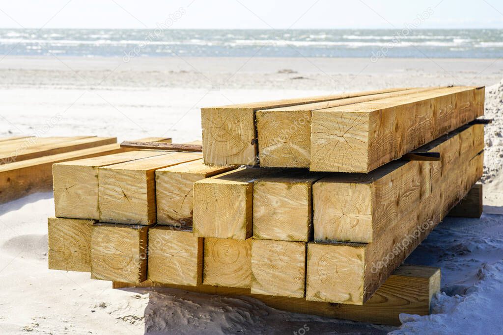 End view of stacked impregnated square wooden pine beams on a sandy beach by Baltic Sea