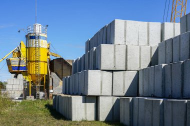 Fabrika bahçesinde bir sürü büyük beyaz beton küp şekilli bloklar ve sarı çimento tankı var.