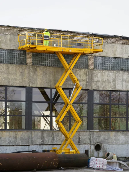 Yellow self propelled scissor lift in action and worker in uniform and safety protective equipment on it