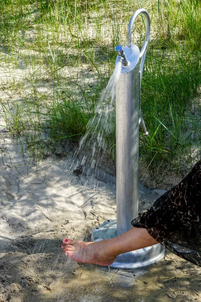 Place for washing the feet on the beach, water drops spraying over woman\'s feet with painted nails