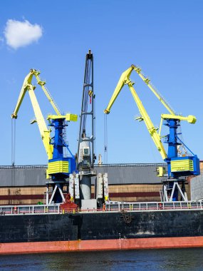 Port cranes painted in the colors of the Ukrainian flag, yellow and blue, blue sky background