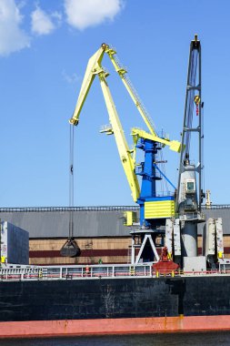 Port crane with bulk cargo bucket painted in the colors of the Ukrainian flag, yellow and blue, blue sky background