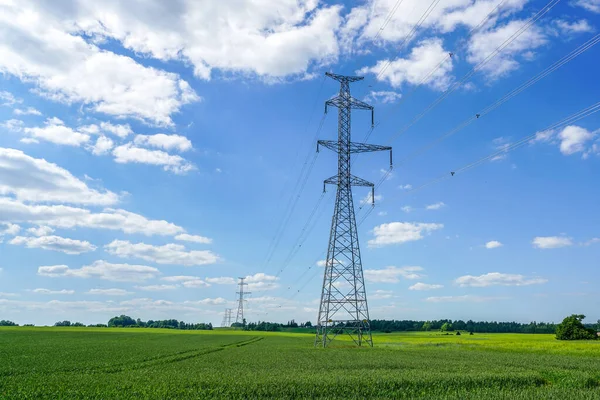 High-voltage power transmission line pylons in a cereal field on a background of blue sky and white clouds