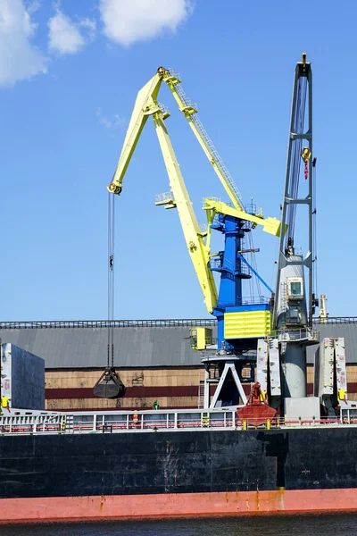Port crane with bulk cargo bucket painted in the colors of the Ukrainian flag, yellow and blue, blue sky background