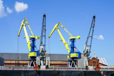 Port cranes painted in the colors of the Ukrainian flag, yellow and blue, blue sky background