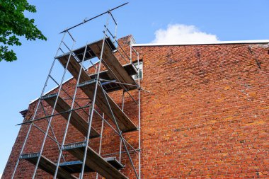 Ön cephe onarımı için eski bir kırmızı tuğla evin duvarının yanında yüksek iskele, mavi gökyüzü arka planı.