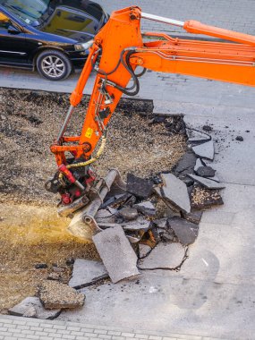 Bir kazıcı, eski asfalt tabakasını şehirdeki tamirat sırasında bir kovayla kırıyor.