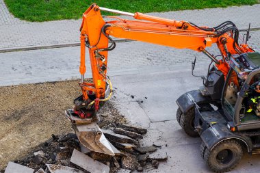 Bir kazıcı, eski asfalt tabakasını şehirdeki tamirat sırasında bir kovayla kırıyor.