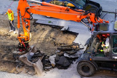 Bir kazıcı, eski asfalt tabakasını şehirdeki tamirat sırasında bir kovayla kırıyor. Kürekle çalışan bir işçi.