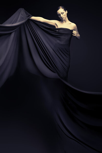 Art fashion photo of a beautiful woman in black dress. Over black background.