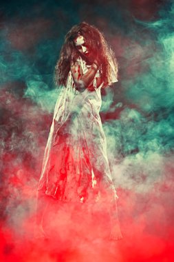 Korkutucu, saplantılı, kana bulanmış, korkunç kırmızı ve yeşil dumanla karanlıkta dikilen bir kadının korku sahnesi. Kana susamış zombi kadın. Korku filmi, gerilim. Cadılar Bayramı.