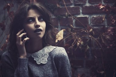 Yıkık bir duvarın arkasında telefonla konuşan solgun gözlü ve tozlu siyah saçlı korkutucu bir hayalet kızın portresi. Boşluğu kopyala.