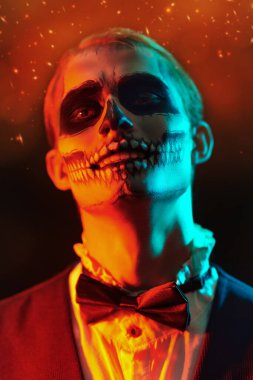 Siyah arka planda gizemli kırmızı ışıklandırmalı kafatası makyajlı yakışıklı bir adam. Dia de los muertos. Ölüler Günü. Cadılar Bayramı.