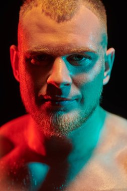 Çok renkli ışıklandırmada siyah bir arka planda yüzü ter içinde kalmış güçlü kızıl saçlı bir atletik adamın portresini yakından çek. Erkek güzellik konsepti.