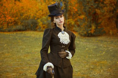 19. yüzyılın koyu siyah takım elbiseli, kendinden emin ve sofistike bir bayan bir sonbahar parkının arka planına karşı poz veriyor..