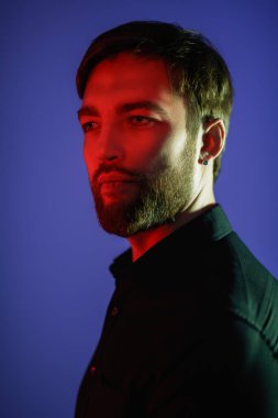 Yüzünde kırmızı ışıkla mavi bir arka planda poz veren orta yaşlı, yakışıklı bir adamın portresi. İş adamı portresi. Erkek modası.