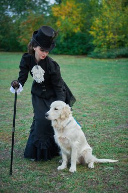 19. yüzyıldan kalma siyah takım elbiseli güzel bir bayanın parkta yürürken av köpeğini okşamasının portresi. Tam boy portre.