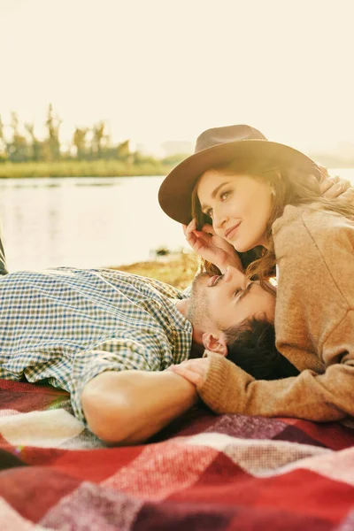 Sweet and tender love. Portrait of a beautiful young woman and man on a romantic date lying on the blanket by the river on a wonderful sunny day.