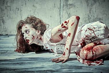 A creepy, devil-possessed woman with pale eyes and tousled hair covering her face and a bloody nightie crawls against a concrete wall. Zombie woman. Horror, thriller. Halloween. clipart