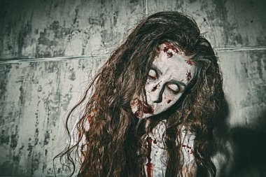 Portrait of a bloodthirsty zombie woman with faded eyes stands against a concrete wall smeared with blood. Devil possessed woman. Horror, thriller. Halloween.  clipart
