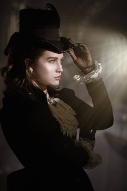 19. yüzyıldan kalma takım elbiseli güzel bir bayan karanlık bir odada parlak mistik bir ışığa bakıyor. Tarihsel saç stili ve makyaj. Vampirler. Cadılar Bayramı.