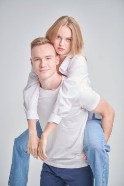 Eğlence ve rahatlık. Mutlu gülümseyen genç adam sevgili kız arkadaşını sırtında taşıyor. Beyaz stüdyo geçmişi. Aşk ilişkisi. 