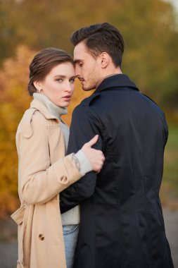 Tutkulu bir aşk. Güz parkının arka planında birbirlerine sarılan zarif sonbahar kıyafetleri içinde güzel ve genç bir çift.. 
