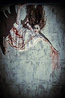 Portrait of a creepy, devil-possessed woman with pale eyes and tousled hair wearing  bloody nightie slides down the blood-covered wall. Zombie woman. Halloween. Copy space. clipart