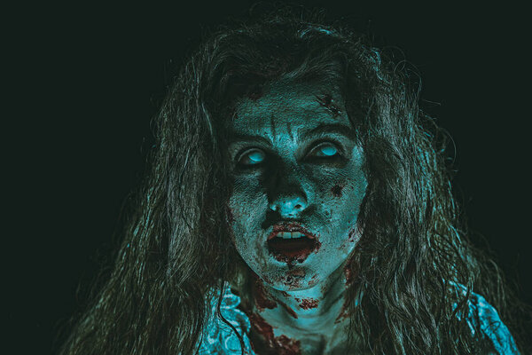 Portrait of a bloodthirsty zombie woman with faded eyes looking up and opening her bloody mouth. Devil possessed woman. Horror, thriller. Halloween. 
