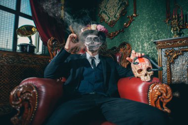 Dia de los muertos. Ölüler Günü. Zarif ve tehlikeli Baron Samedi eski bir kalede puro içiyor. Kafatası şekeri makyajlı yakışıklı adam. Cadılar Bayramı.