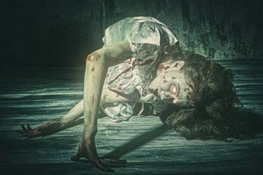 Şeytan tarafından ele geçirilmiş korkunç bir kadın kanlı geceliğiyle beton bir duvarın arkasına eğiliyor. Ürkütücü zombi kadın. Korku, gerilim. Cadılar Bayramı.